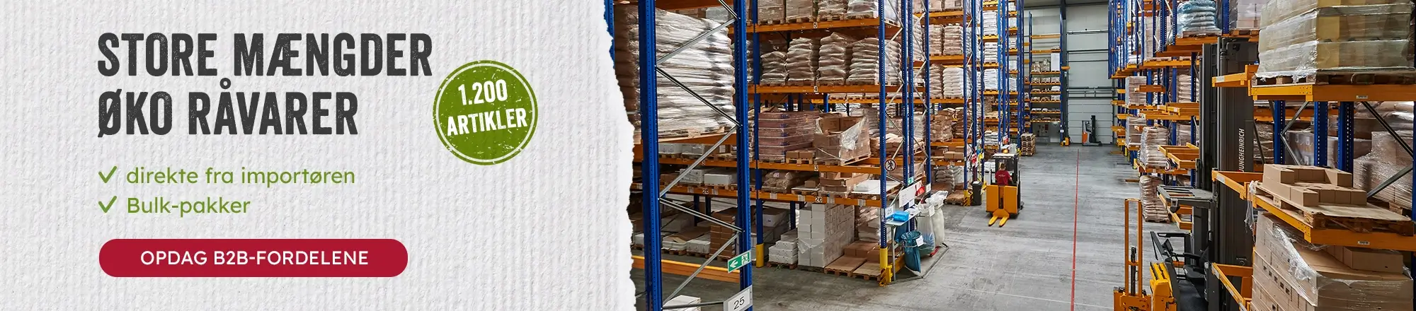 Indvendigt billede af en lagerhal med høje reoler fyldt med paller og kasser samt gaffeltrucks, klar til levering af økologiske råvarer