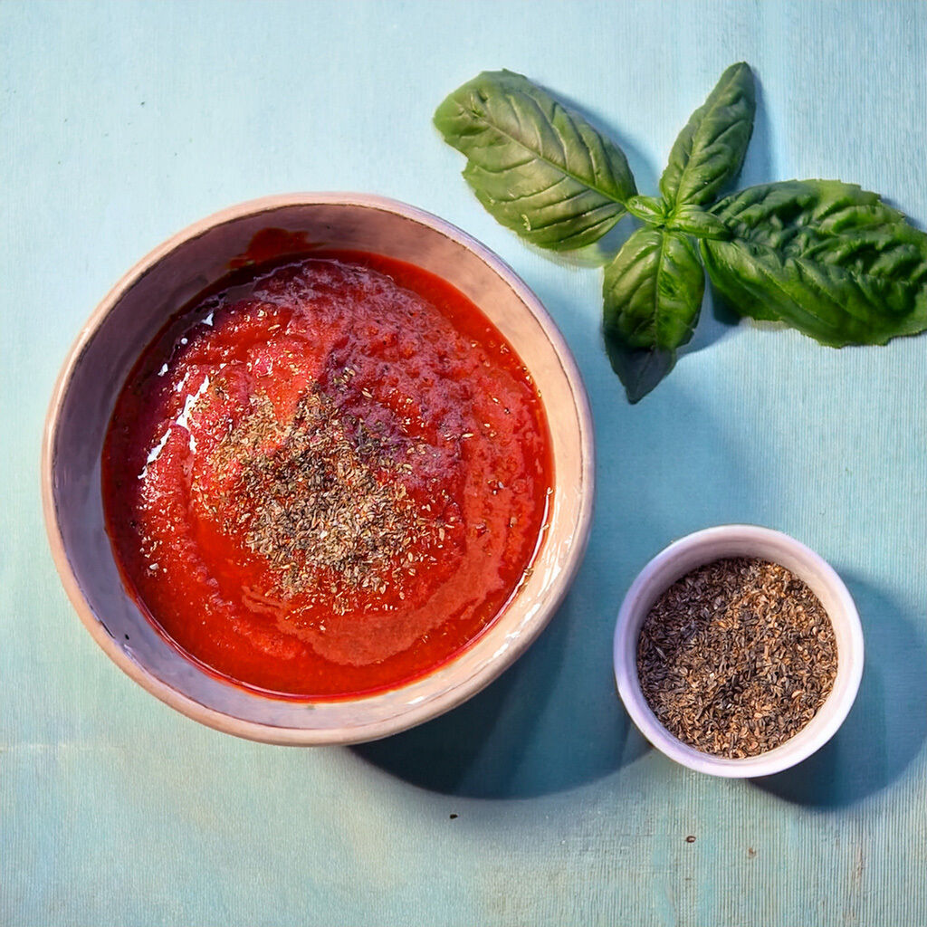 En skål med frisk tomatsauce pyntet med krydderurter, ledsaget af friske basilikumblade og en lille skål med tørrede krydderurter.