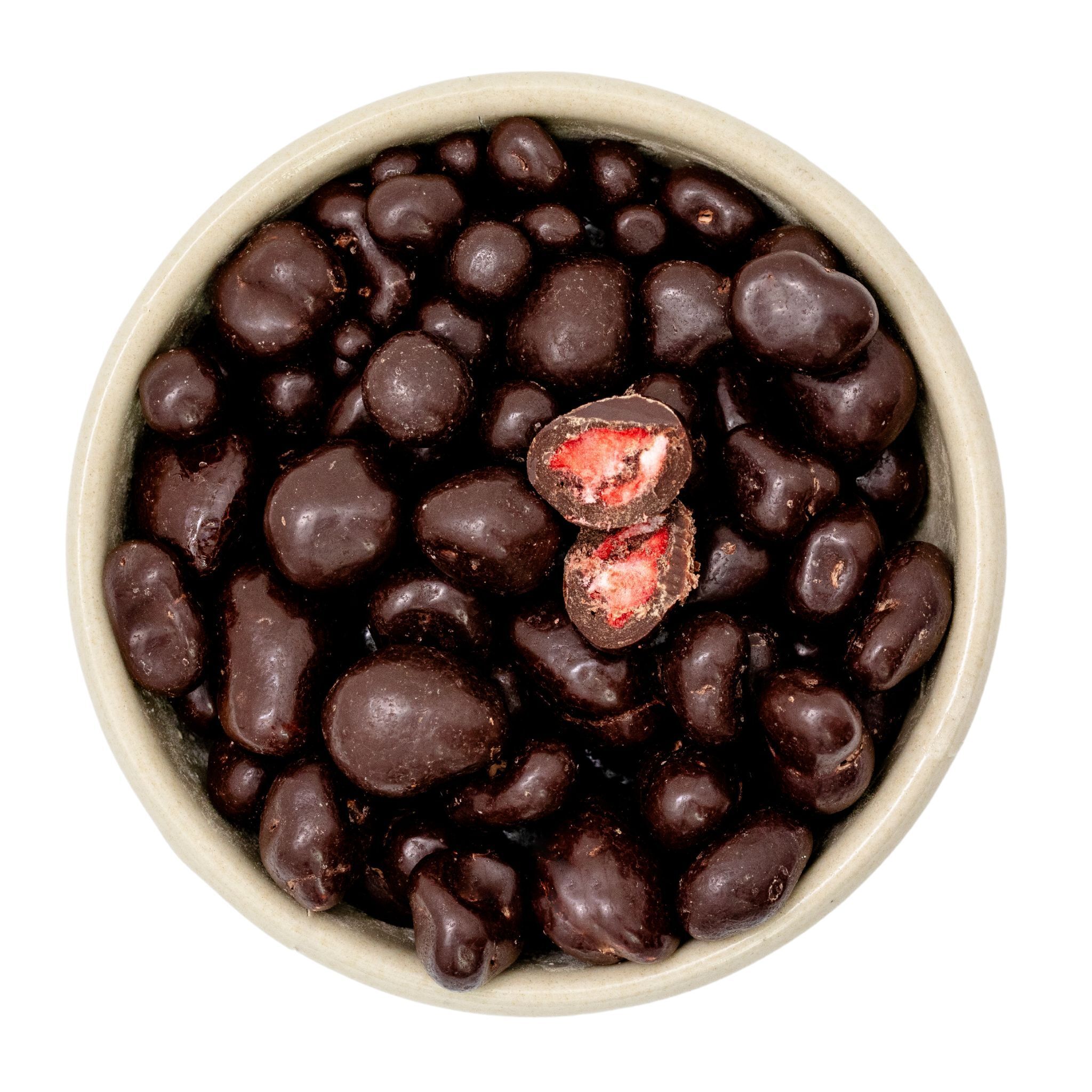 Vogelperspektive auf eine Schale mit unregelmäßig geformten, dunkel schokoladenüberzogenen gefriergetrockneten Erdbeeren; in der Mitte zwei halbierte Stücke, die das rote Innere zeigen.