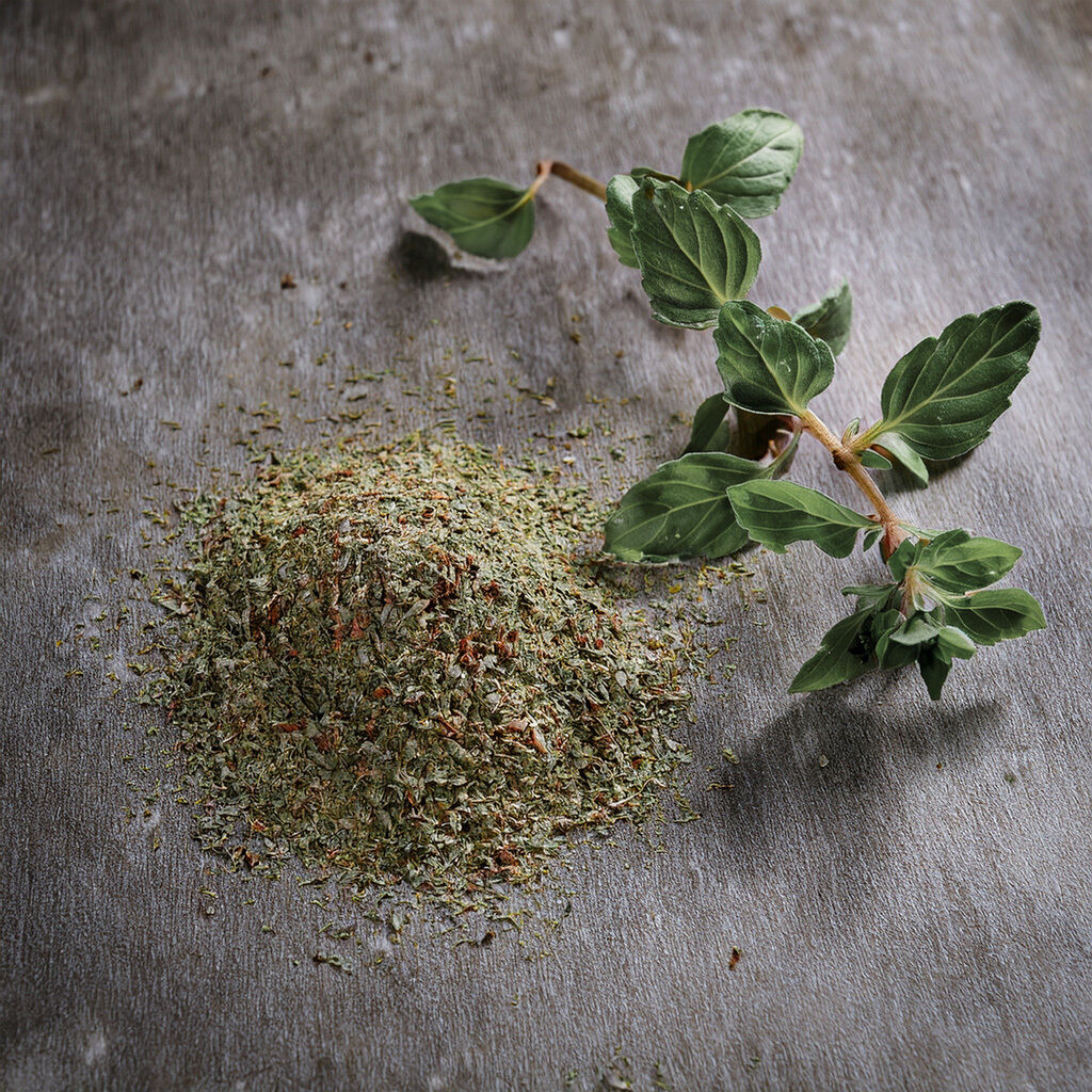 A pile of dried oregano leaves next to a fresh oregano sprig on a wooden surface