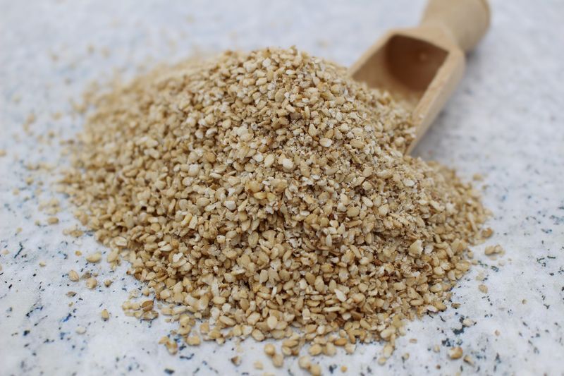 Bunke groft hakkede sesamfrø på et lyst underlag med en lille træske.