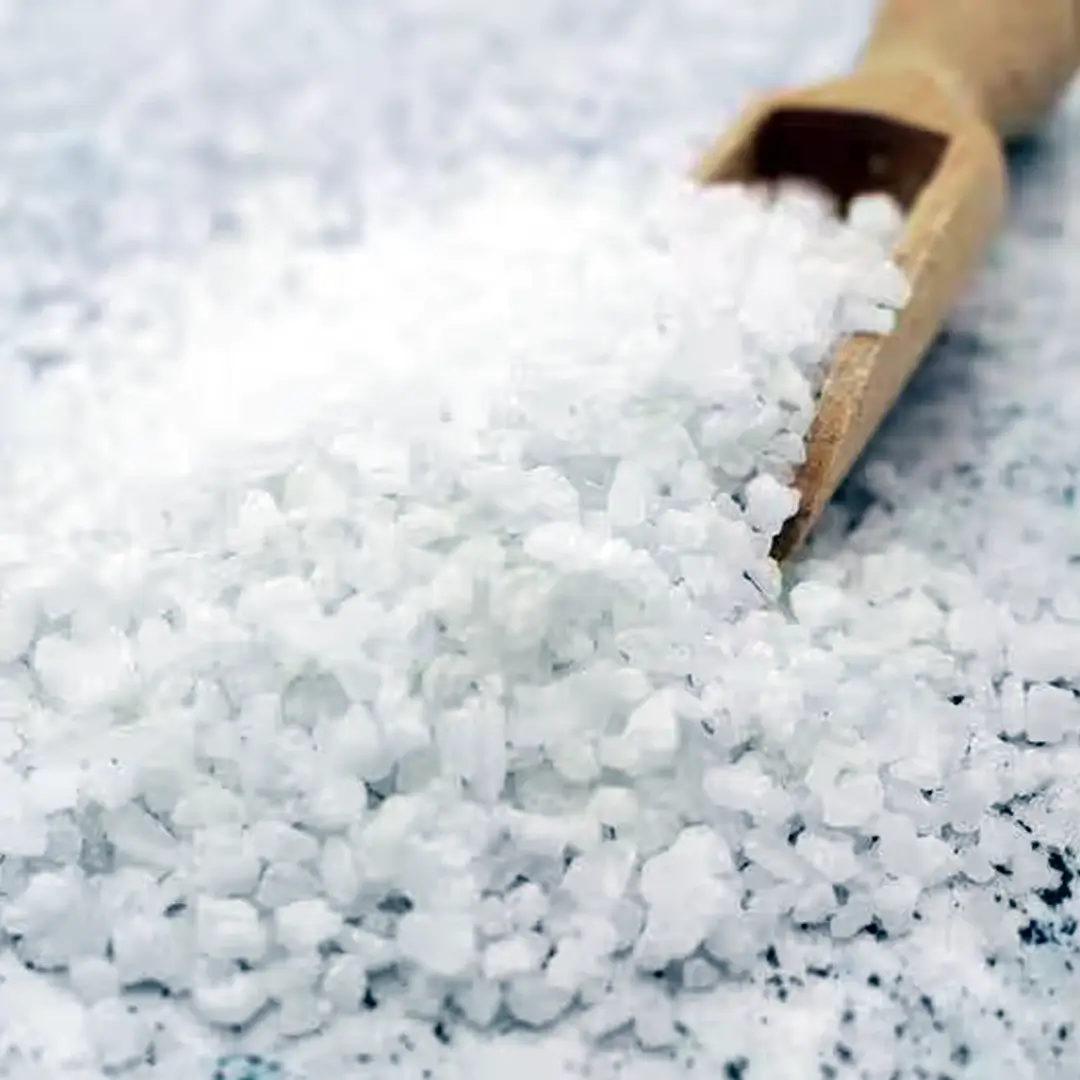 Nærbillede af grove hvide havsaltsflager i en træske på en lysegrå overflade