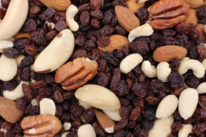 Nærbillede af en blanding af tørrede rosiner og forskellige nødder: cashewnødder, mandler (inkl. afskallede mandler), pekannødder og paranødder.