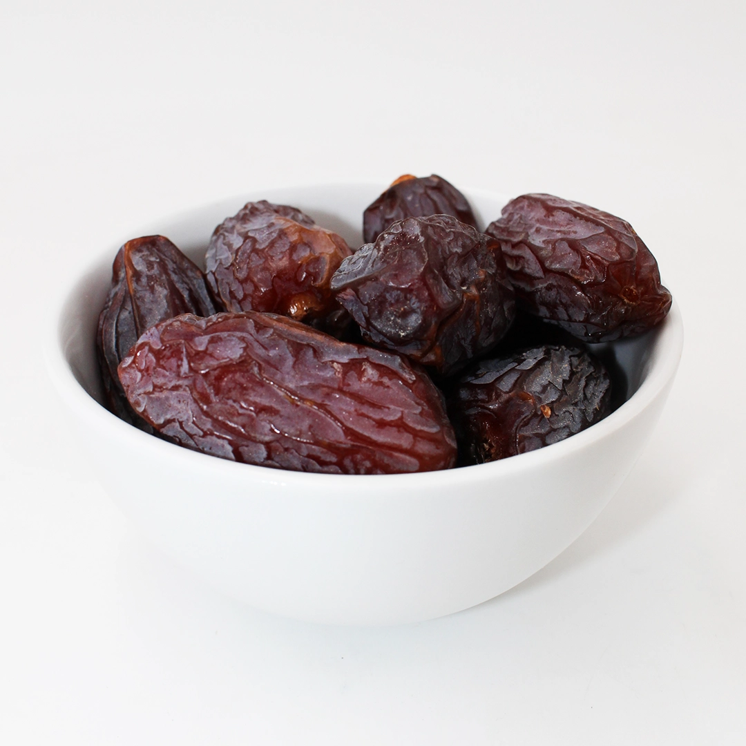 Nærbillede af en hvid skål fyldt med mørke, rynkede tørrede dadler