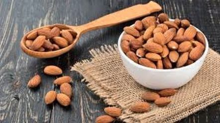 Bowl and scoop of whole almonds on wooden table