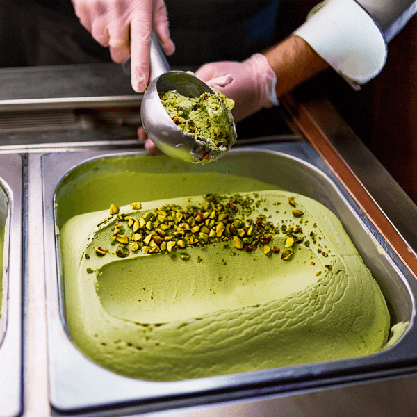 Hand scooping pistachio gelato topped with nuts