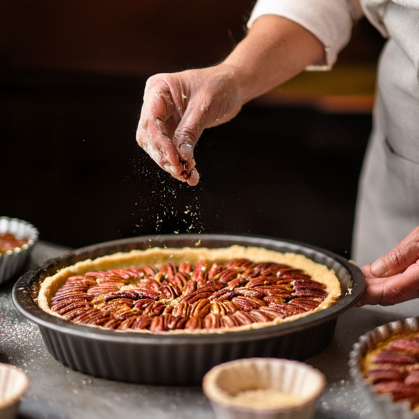 Hands sprinkling sugar over pecan tart
