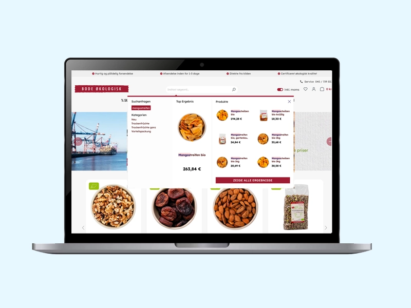 Åben bærbar computer på lyseblå baggrund, der viser en e-handelswebside med økologiske nødder, mandler, valnødder og tørret frugt