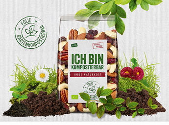 Komposterbar pose med blandede økologiske nødder og tørret frugt, mærket 'ICH BIN KOMPOSTIERBAR', omgivet af jord, grønne planter, blomster og et kompost-ikon.