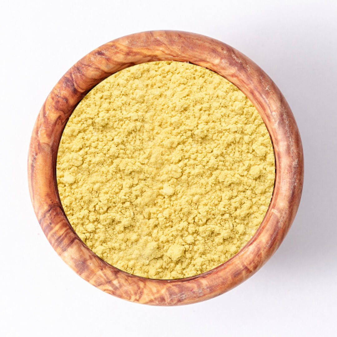 Top view of a wooden bowl filled with organic mustard powder on a white background
