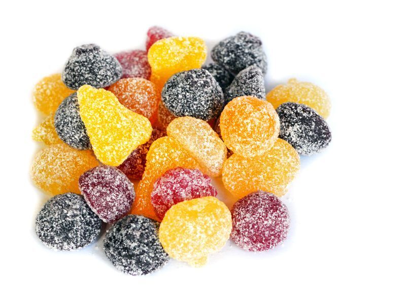 Billede af sukkerbelagte vingummier i forskellige farver (gul, orange, rød og sort) på hvid baggrund