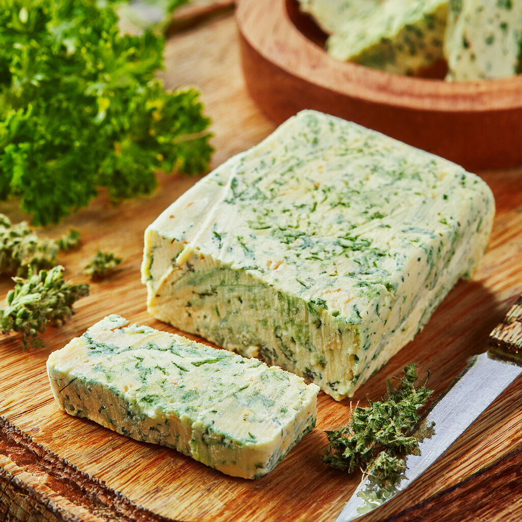 A block of fresh herb butter on a wooden board with a knife and herbs