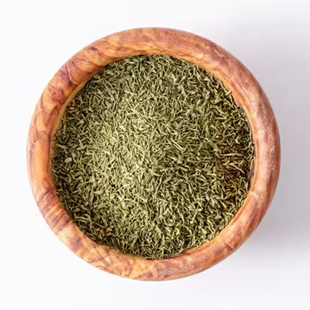 Rund træskål fyldt med fint snittede tørrede krydderurter (grønne) på hvid baggrund, set ovenfra