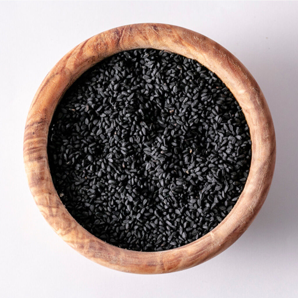 Billede taget oppefra af sorte sesamfrø i en rund træskål på hvid baggrund