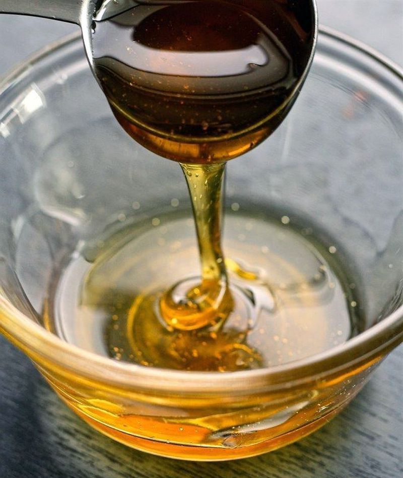 Nahaufnahme: Löffel gießt goldenen Honig in eine Glasschale