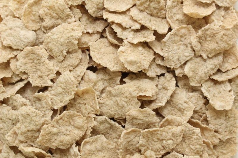 Nahaufnahme knuspriger Vollkorn-Weizenflocken: trockene, gebrochene Frühstücksflocken mit rauer Textur