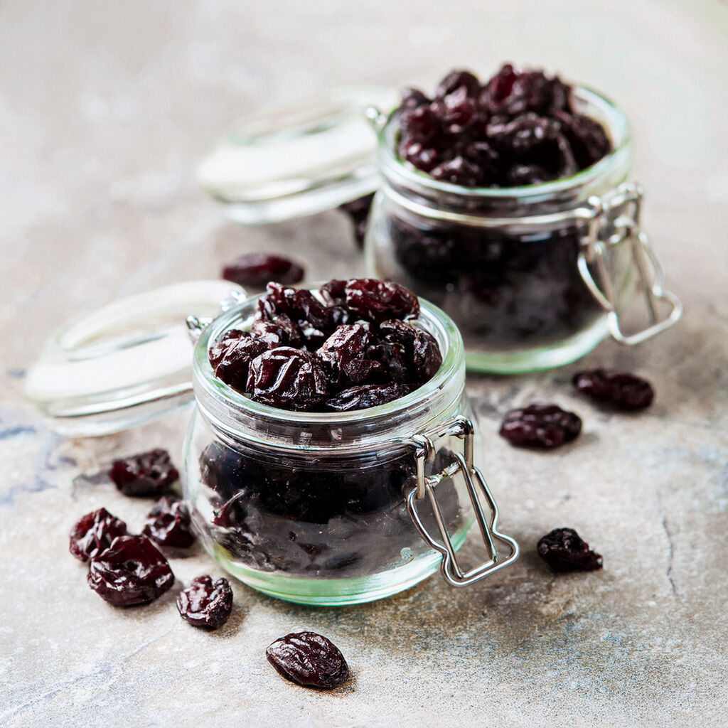 To glasbøtter fyldt med tørrede mørke druer på en tekstureret overflade