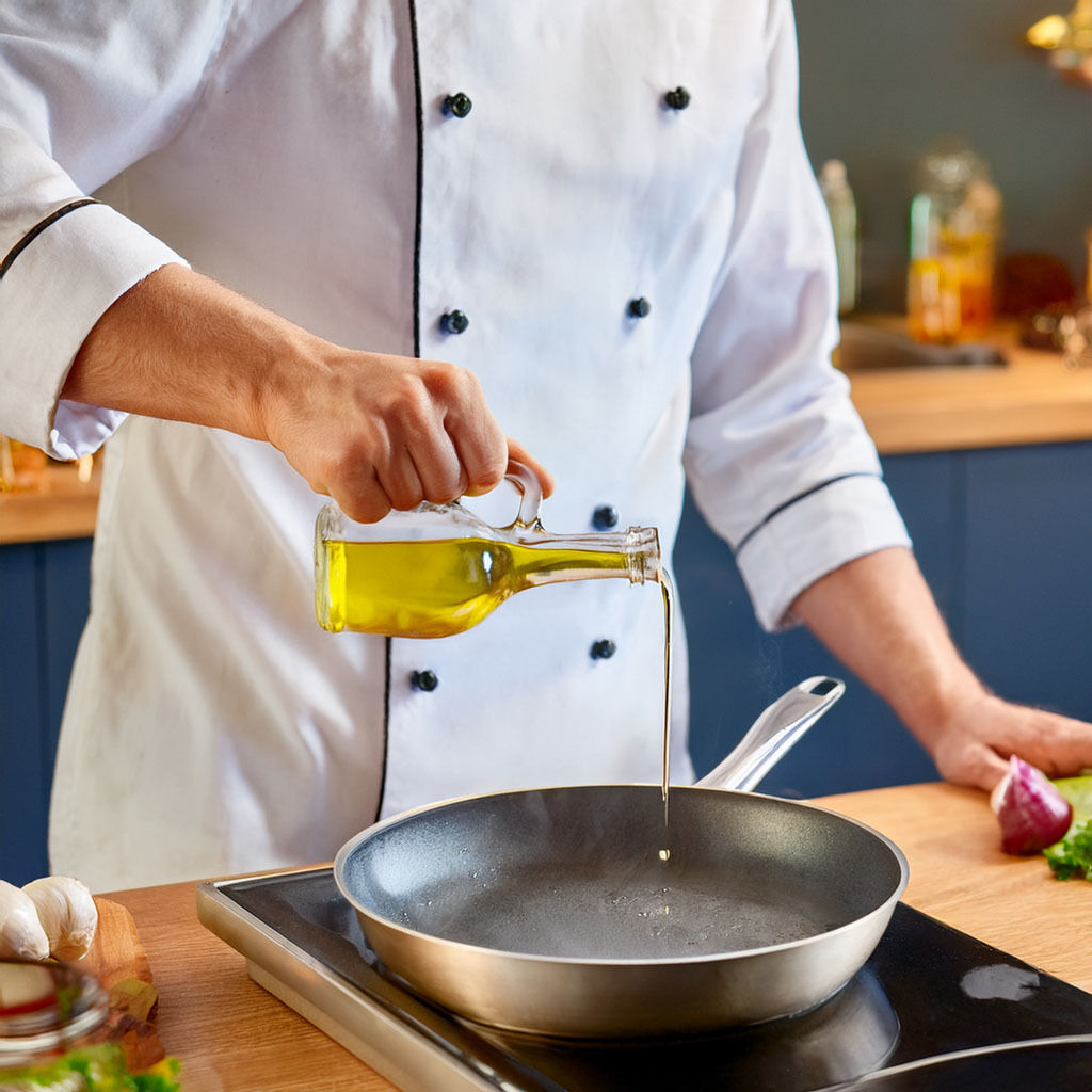 Chef pouring olive oil into frying pan