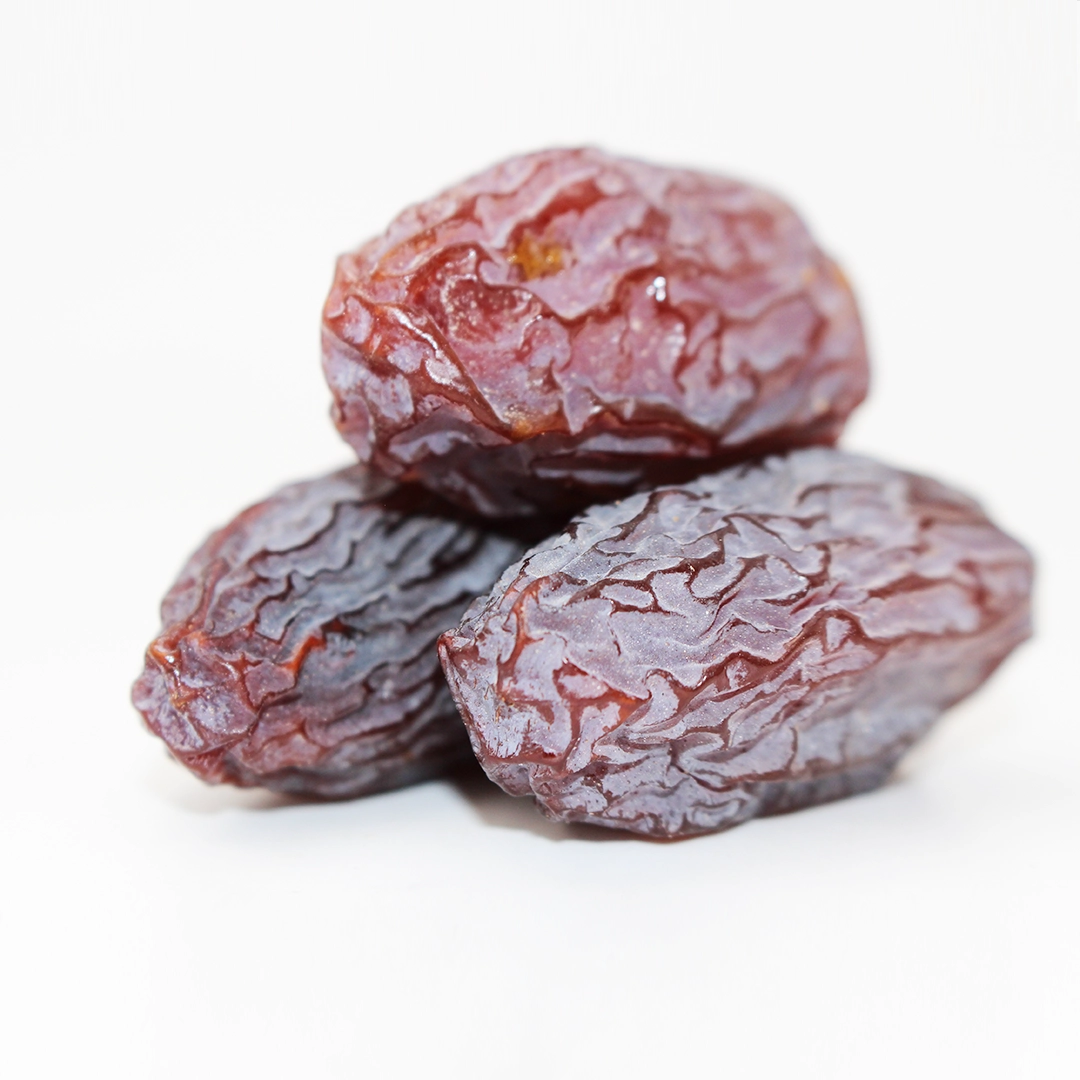 Nærbillede af tre tørrede dadler med rynket, blankt brunt skind på hvid baggrund