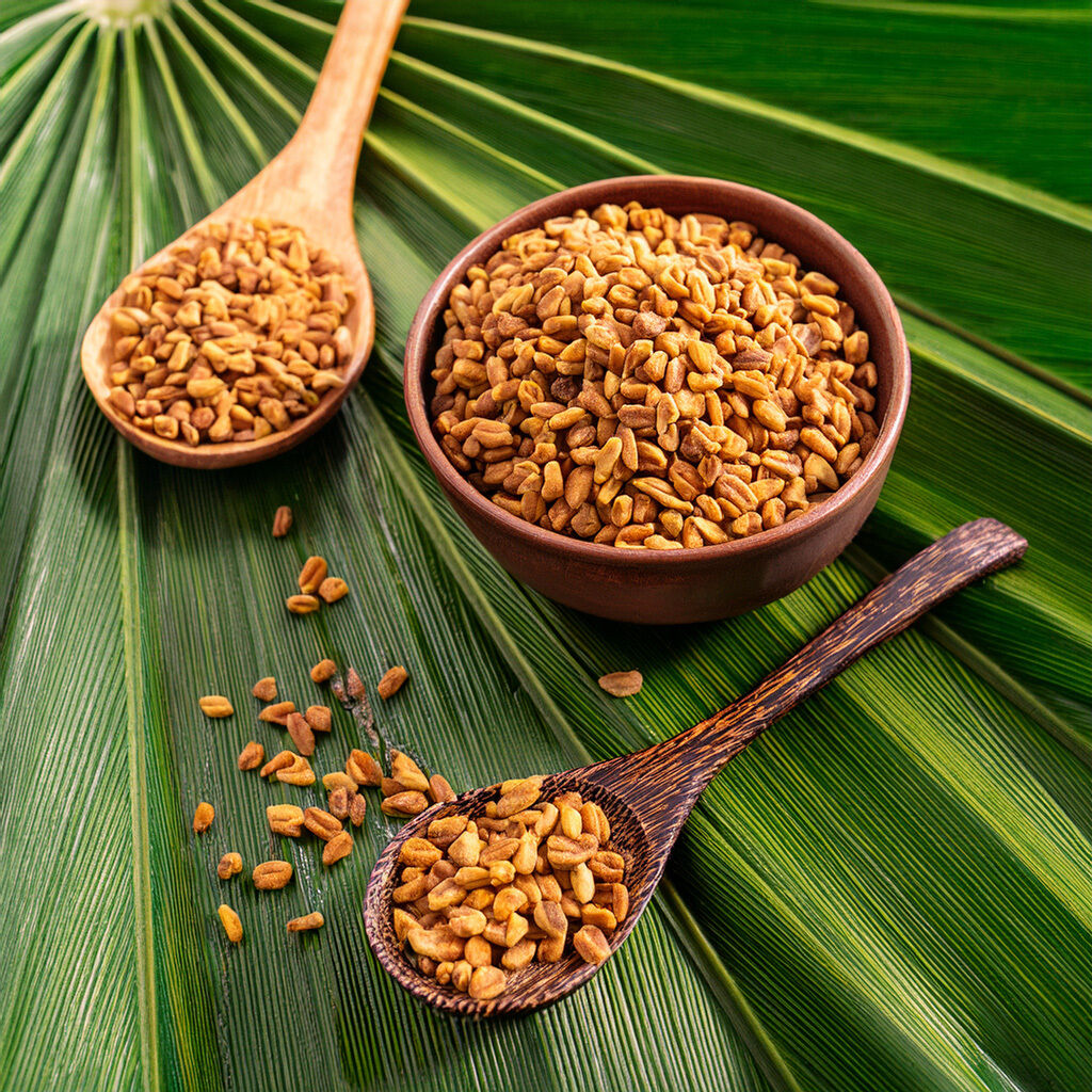 Skål og træske med gyldne, ristede bukkehornsfrø lagt på store grønne blade