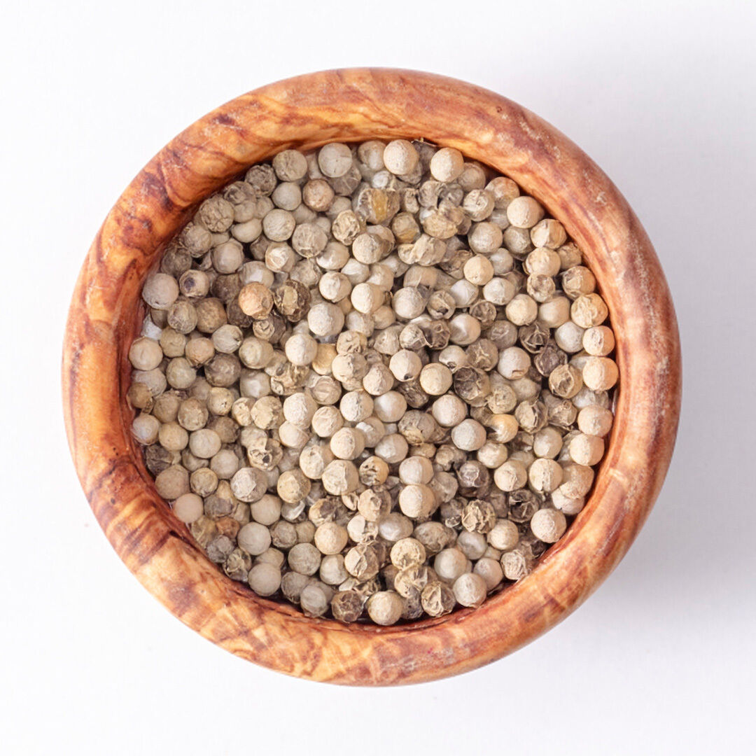 Wooden bowl filled with whole white peppercorns on a white background