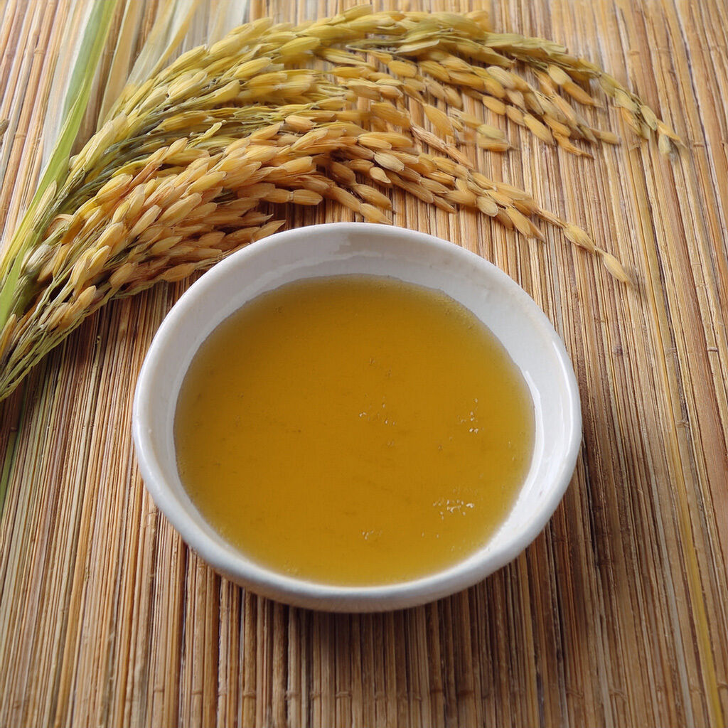 Skål med gylden risolie og risaks på bambusmåtte