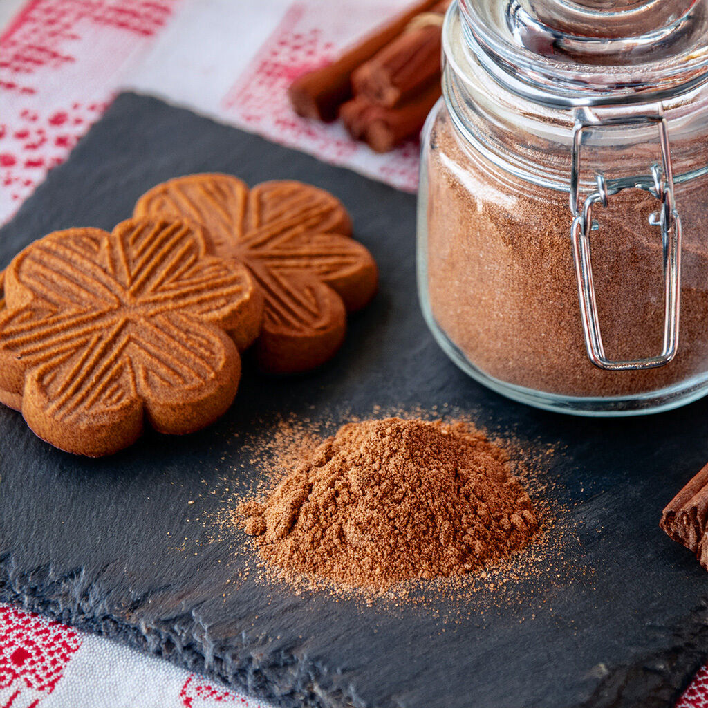 Glas mit gemahlenem Zimt, eine kleine Menge Zimtpulver und gewürzte Blütenkekse auf Schieferplatte