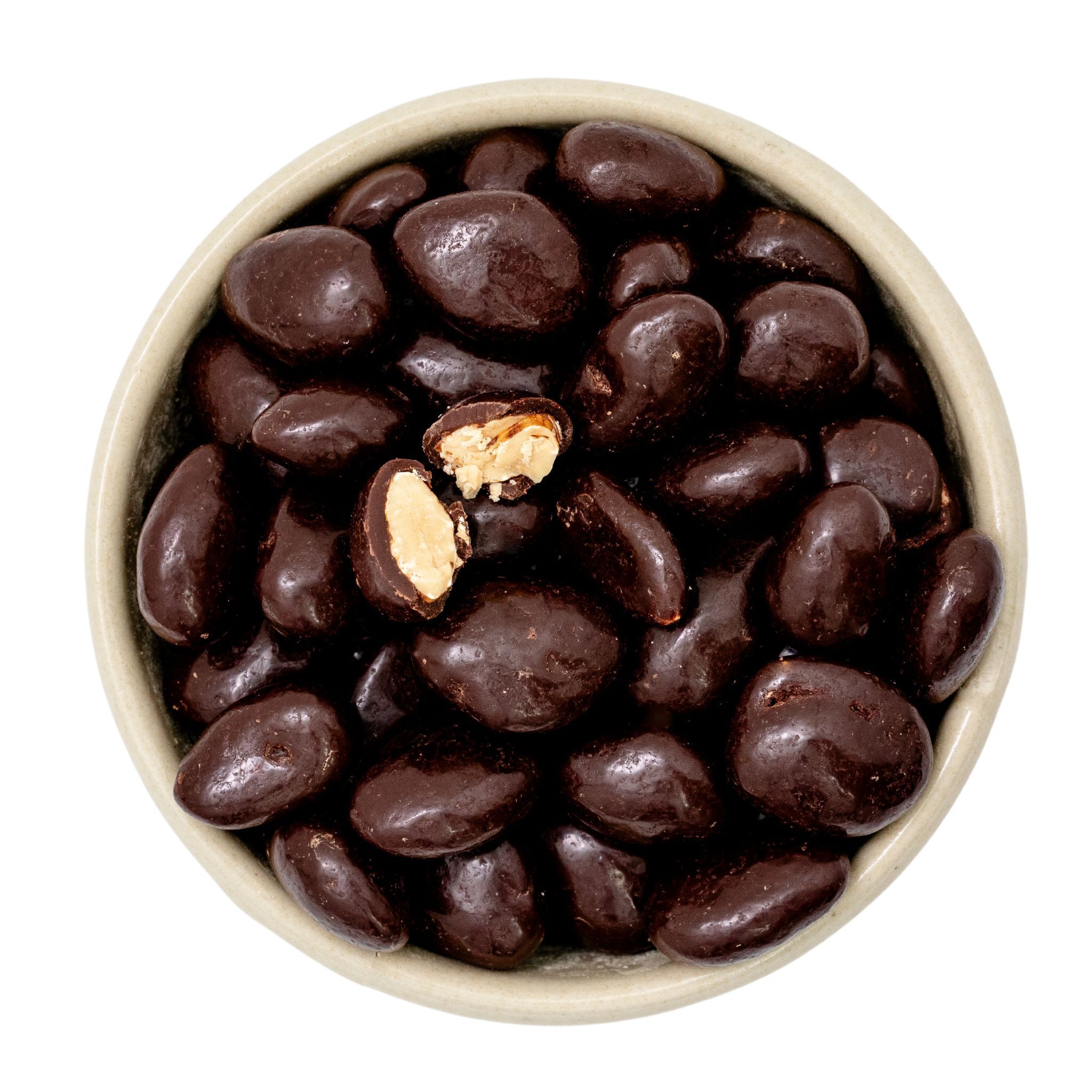 Schale mit dunklen, schokoladenüberzogenen Erdnüssen; eine aufgebrochene Erdnuss zeigt das Innere