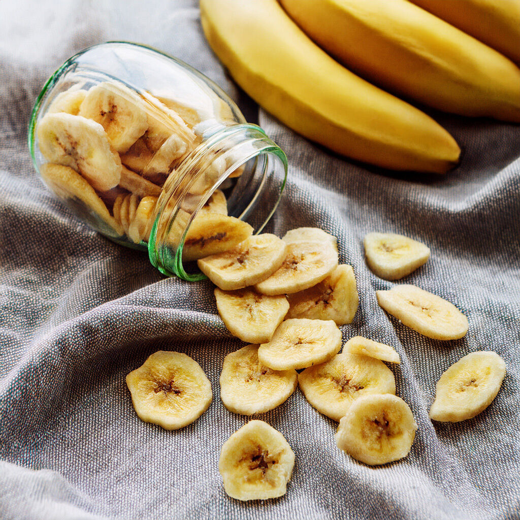 Banana chips spilling from a glass jar on fabric