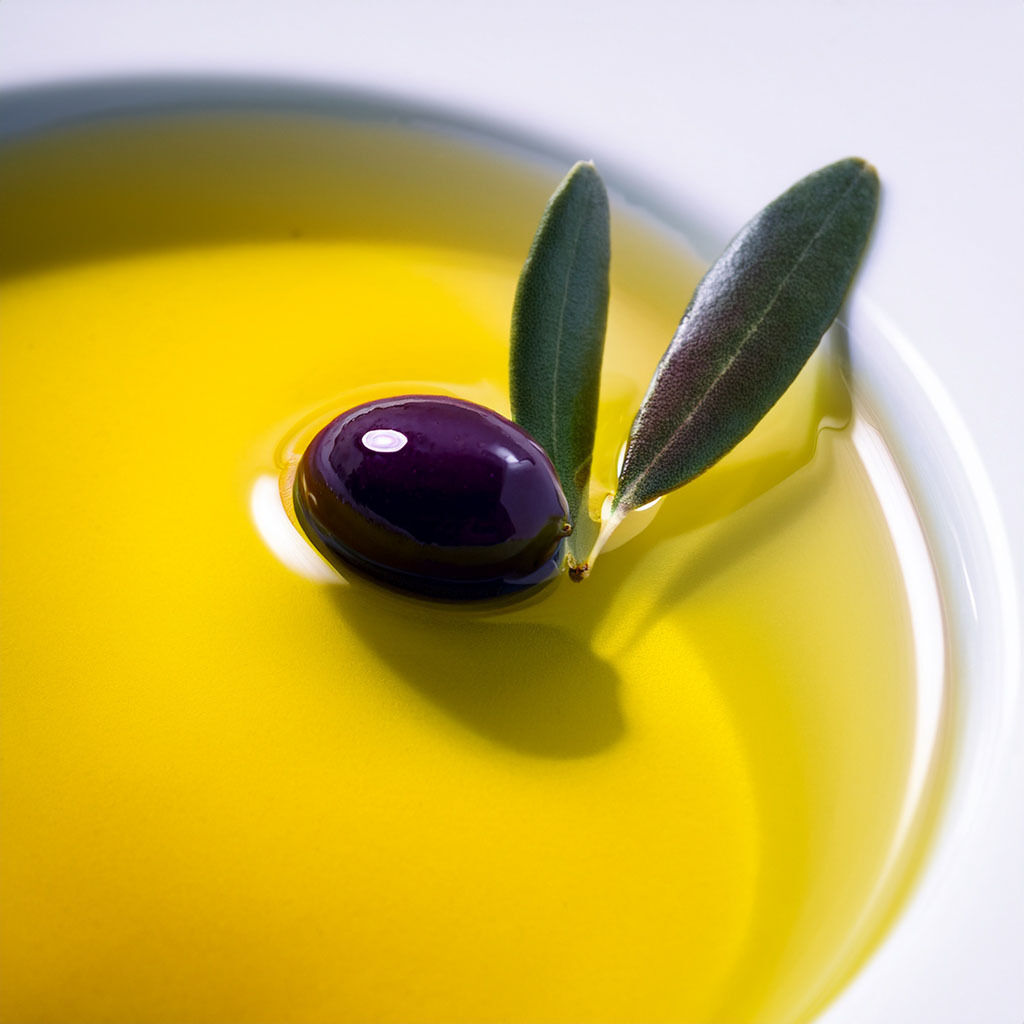 Close-up of a black olive and leaves in olive oil