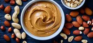 Bowl of creamy peanut butter surrounded by nuts