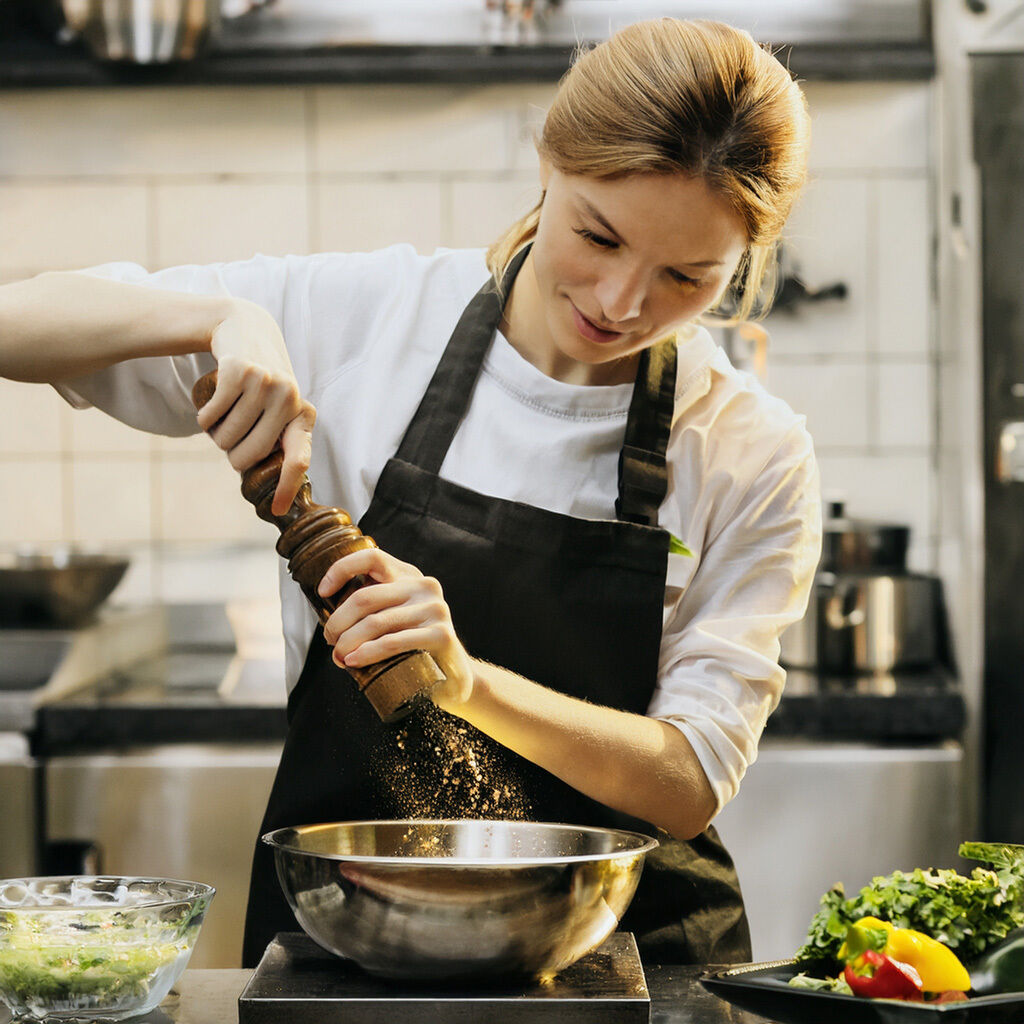 Female chef seasoning food with pepper grinder in a commercial kitchen