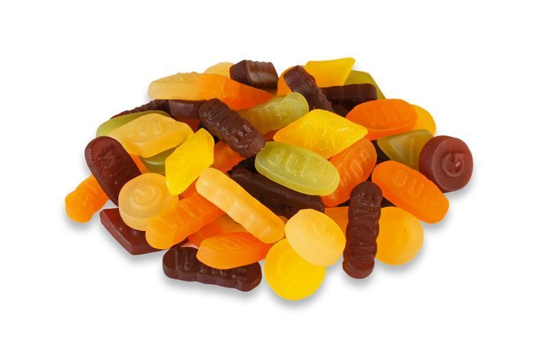 En bunke blandede, farverige vingummier i forskellige former og frugtsmage på hvid baggrund