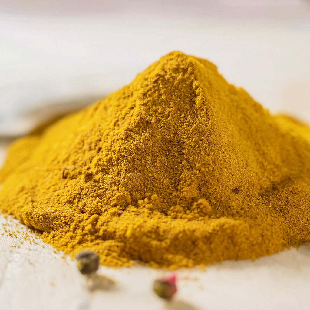 Nærbillede af en bunke gyldent karrypulver på et lyst underlag med et par peberkorn i forgrunden