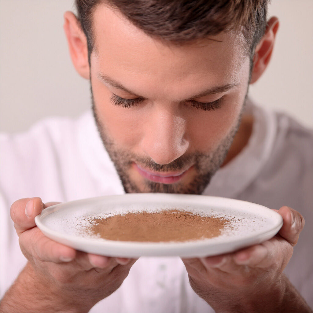 Nærbillede af mand, der holder en hvid tallerken med kanelpulver og dufter til det