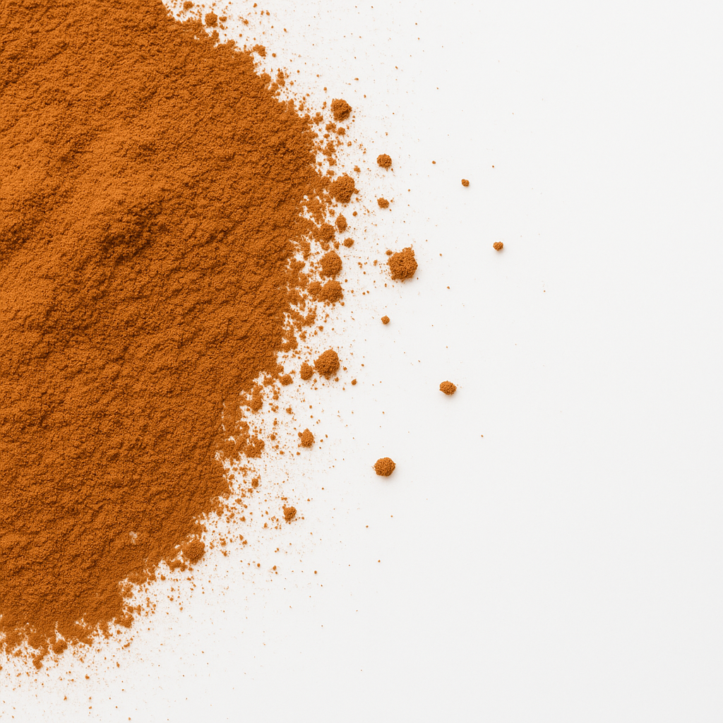Nahaufnahme von gemahlenem Zimt: feines braun-orangenes Pulver mit verstreuten Krümeln auf weißem Hintergrund