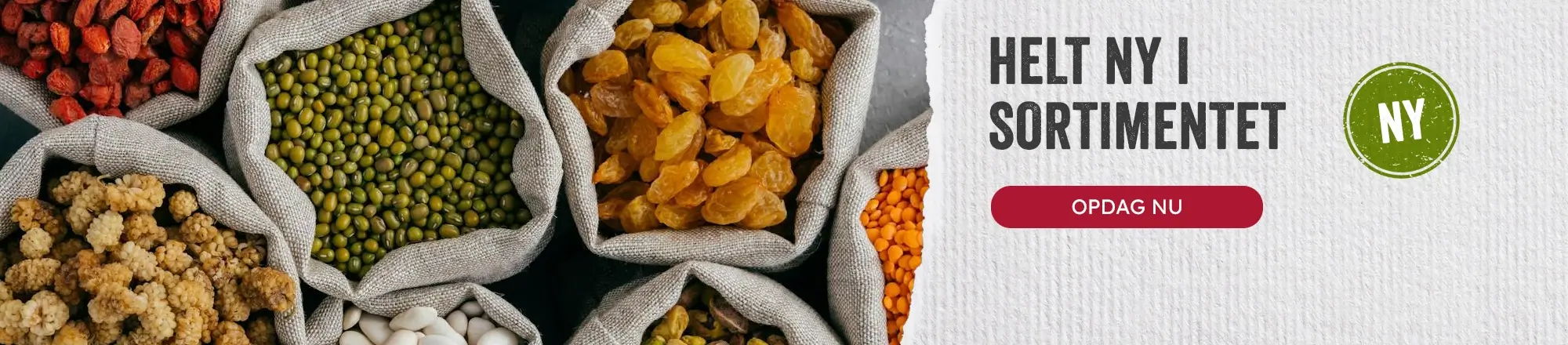Top-down billede af åbne juteposer fyldt med tørrede varer: gule rosiner, mungbønner, røde linser, hvide bønner og tørrede morbær ved siden af reklamebanneret 'Helt ny i sortimentet'.