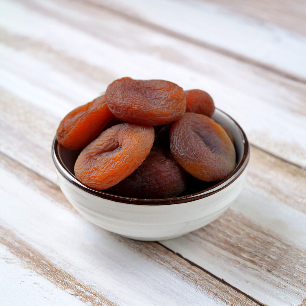 A bowl filled with dried apricots resting on a wooden table.