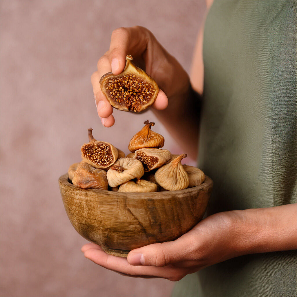 Hand holding halved fig above bowl of dried figs