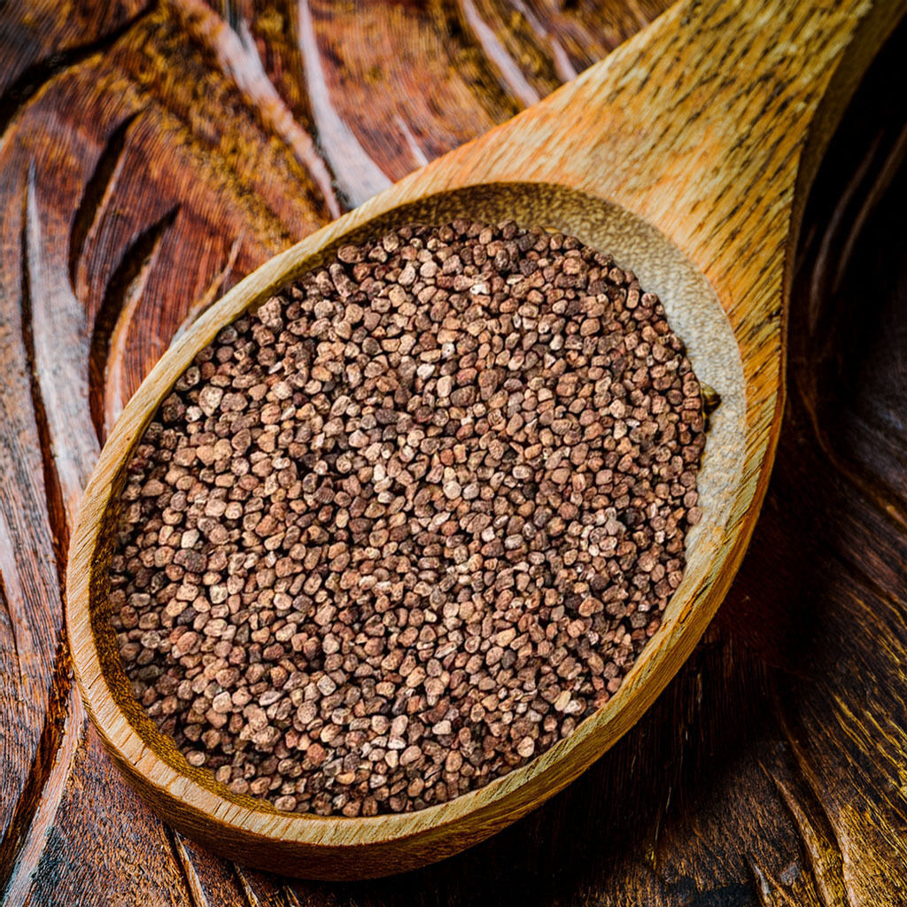 Nærbillede af en træske fyldt med små brune korn lagt på et rustikt træbord