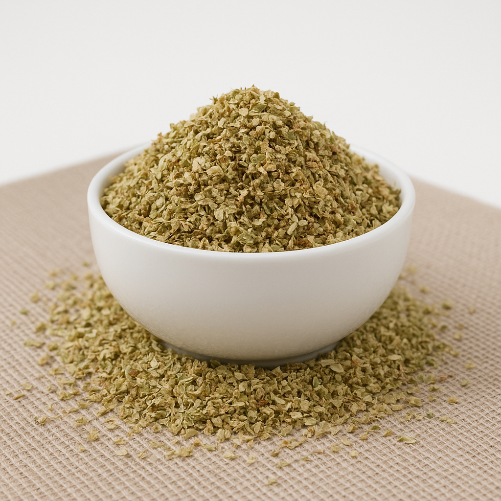 Hvid skål fyldt med tørrede oreganoflager, nogle flager spredt omkring på et lyst bordunderlag