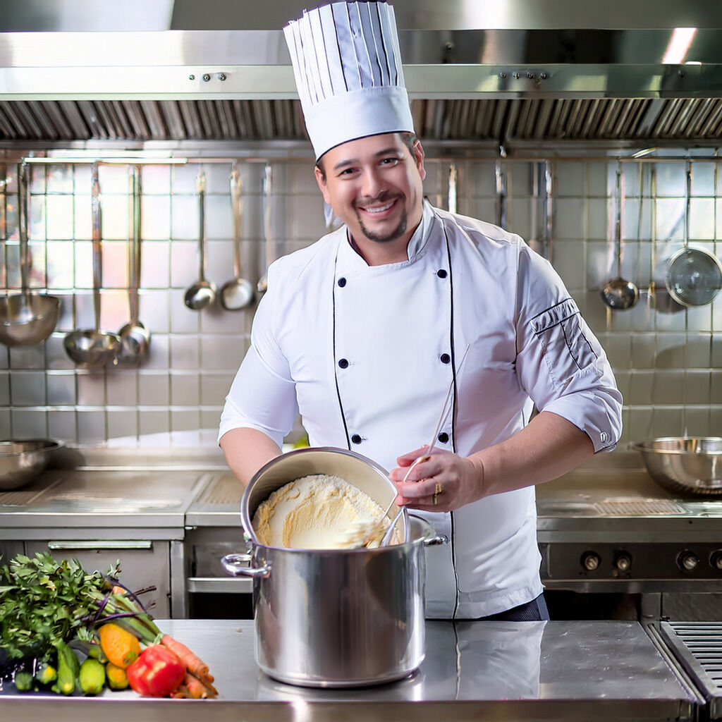 Smiling chef in a white uniform preparing a dish in a commercial kitchen