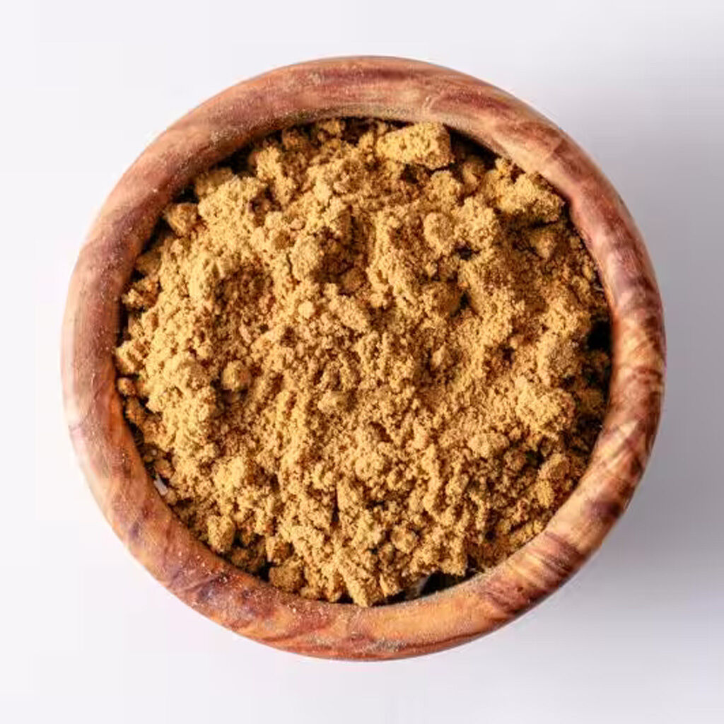 Set oppefra: træskål fyldt med fint, lysebrunt ingefærpulver på hvid baggrund