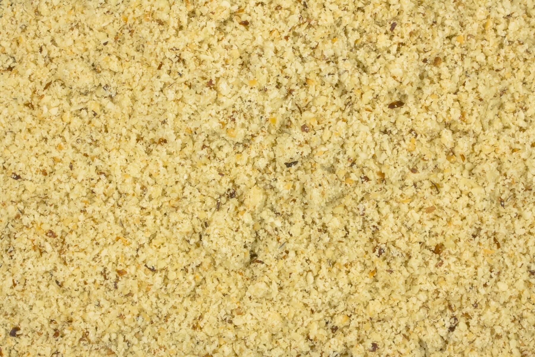 Nahaufnahme von grob gemahlenen Semmelbröseln (Paniermehl) mit kleinen braunen Körnchen, gelblich-beige Struktur