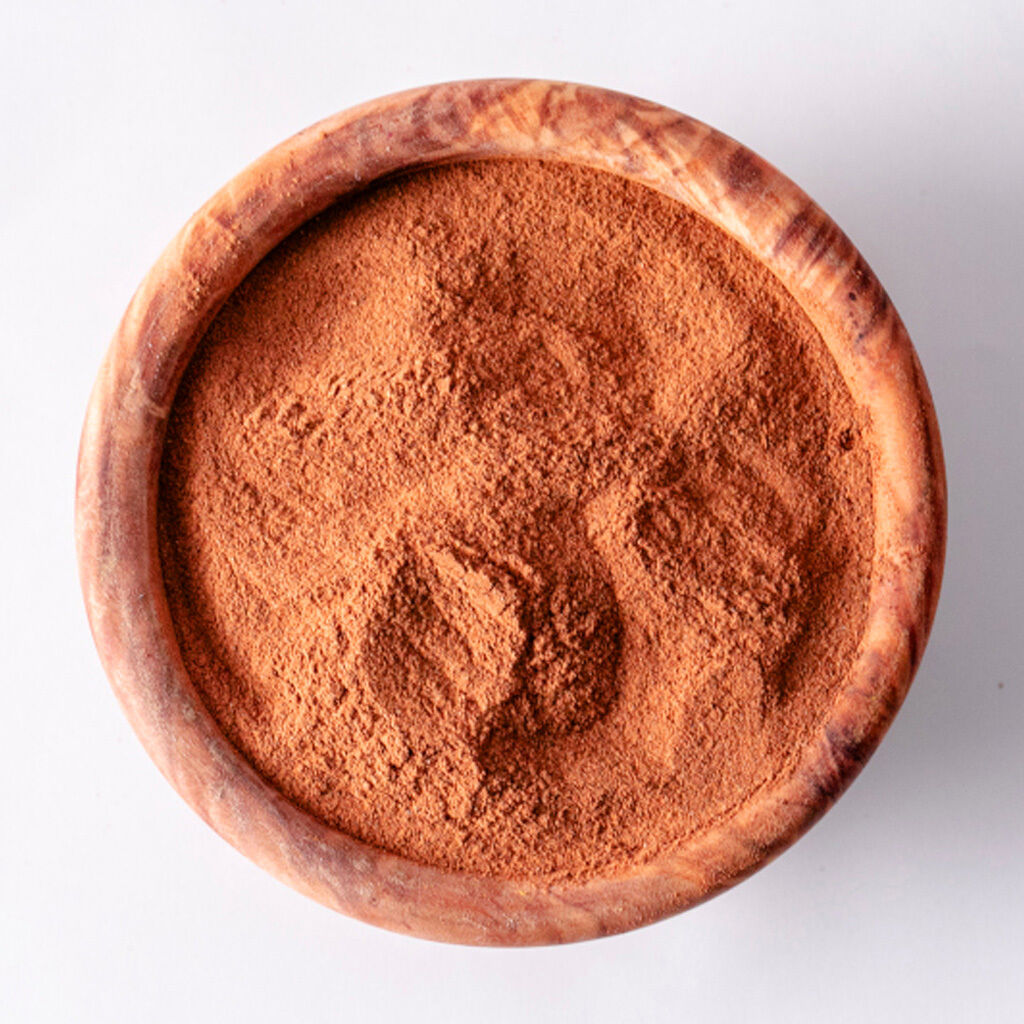 Træskål set ovenfra, fyldt med fint, aromatisk kanelpulver i varm brun nuance