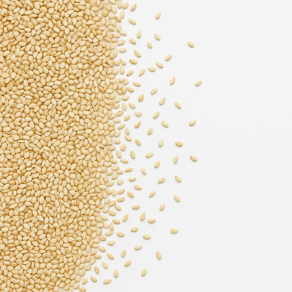 Close-up of hulled sesame seeds scattered on white